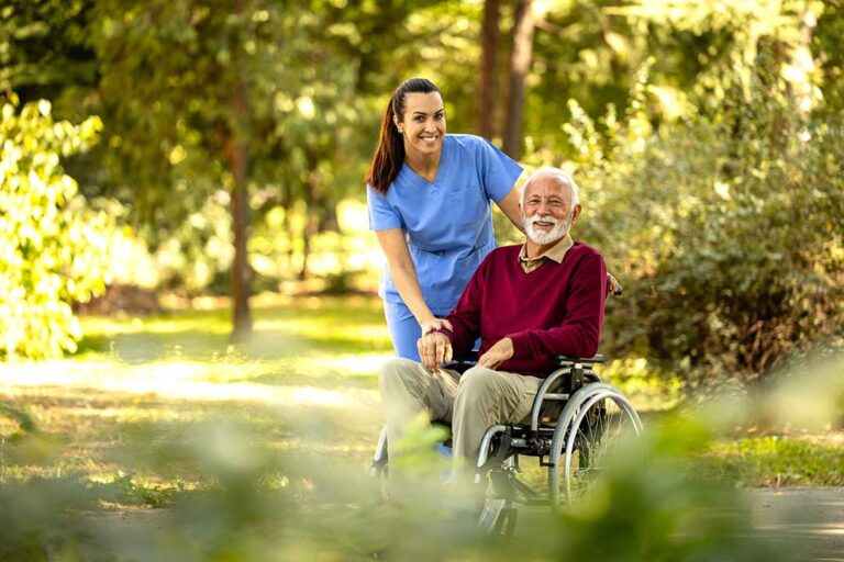 Two older adults talking with a nurse in a bright, comfortable common room.